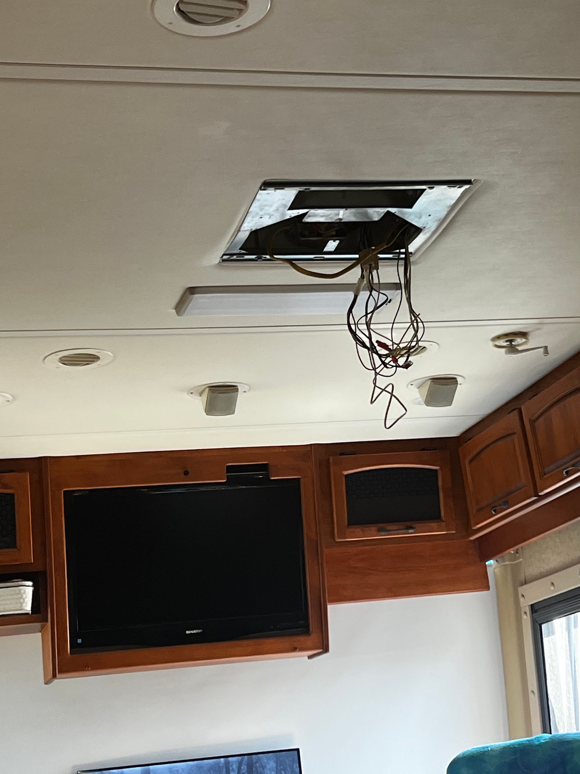 Interior of RV with damaged ceiling vent and exposed wires, television and cabinets below.