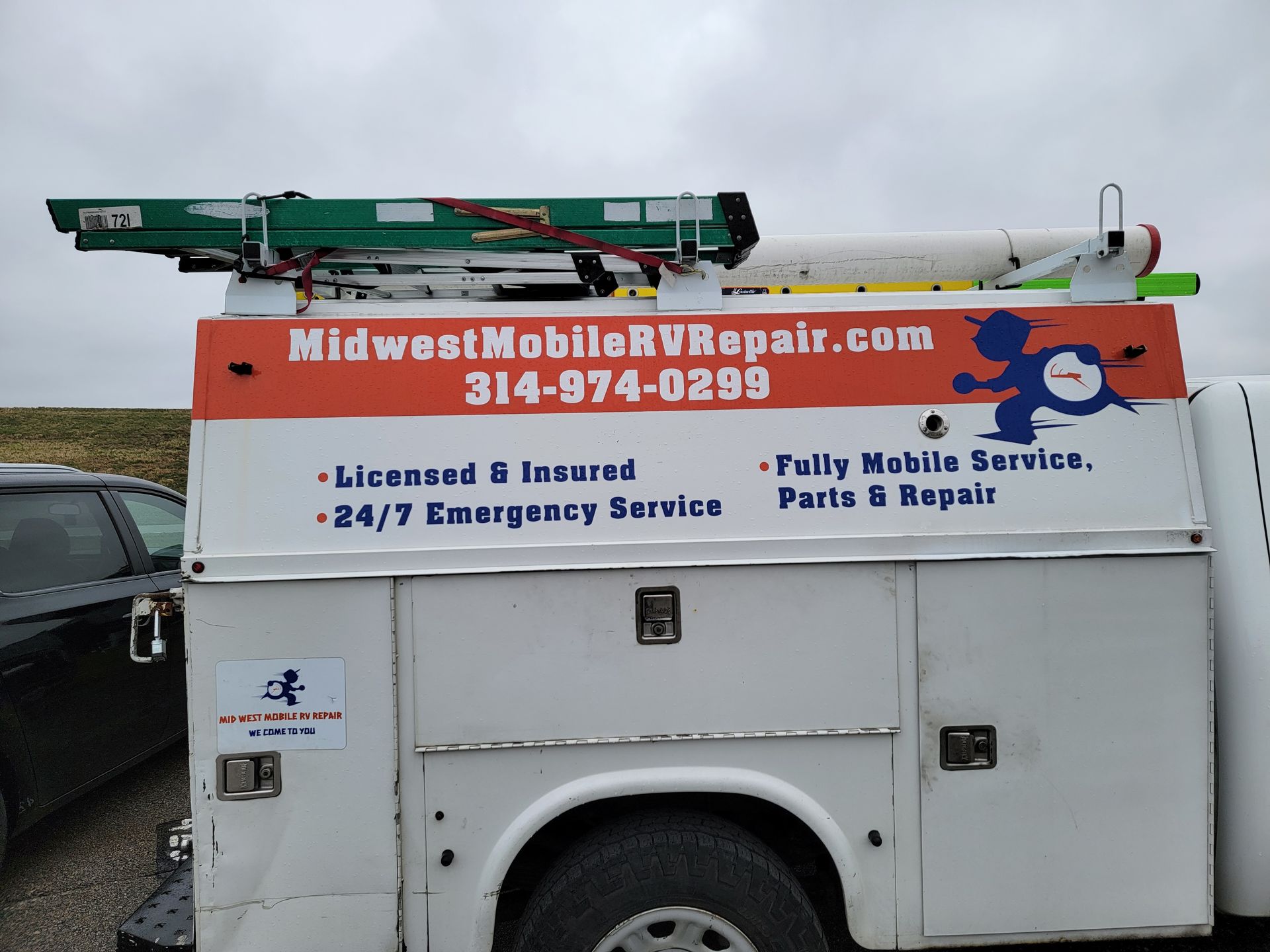 White RV repair truck with MidwestMobileRVRepair.com, ladder, and a cartoon character on top.