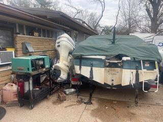 Boat on a trailer with outboard motor, covered by a green tarp. A green generator is nearby.