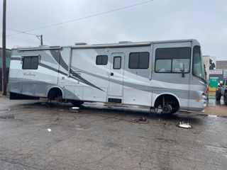 RV with missing wheels parked on a wet, gray surface.