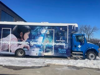 Blue Emerson Mobile Library bus with a child and graphics, parked on snow.