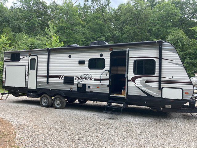 Gray and white camper trailer parked on gravel, with door open and steps visible.