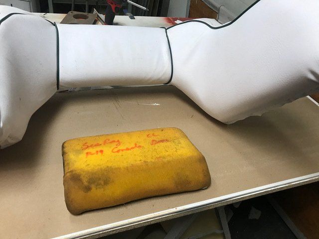 White upholstered automotive headrest with yellow foam pad in workshop setting.