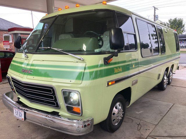 Green and white GMC motorhome parked at a gas station, with green stripes and trim.