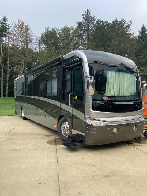 Large, two-toned RV parked on concrete. Silver and brown exterior, awning extended. Step stool deployed.