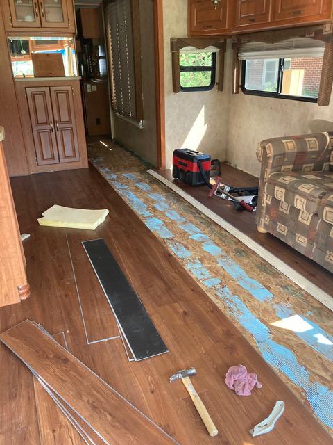 RV interior, flooring renovation in progress; exposed subfloor with tools and planks.