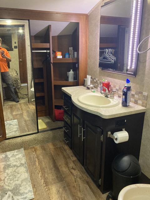 RV bathroom with dark brown cabinets, a large mirror, and a person in the reflection.