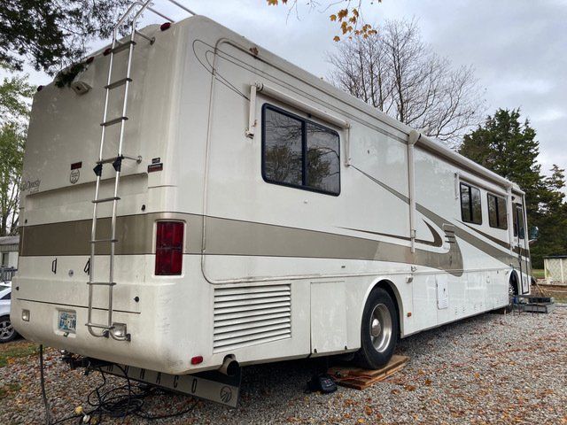 White and beige RV parked outside on gravel, ladder on back, awning extended.