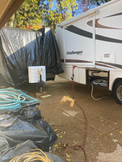 RV next to a covered trailer; a water hose and other gear are on the ground.