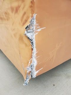 Brown corner of a damaged object; tear reveals grey interior material and white residue.