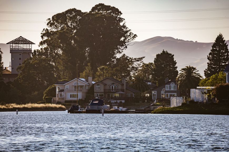 Small boat on rippling water before lakeside houses and trees at sunset