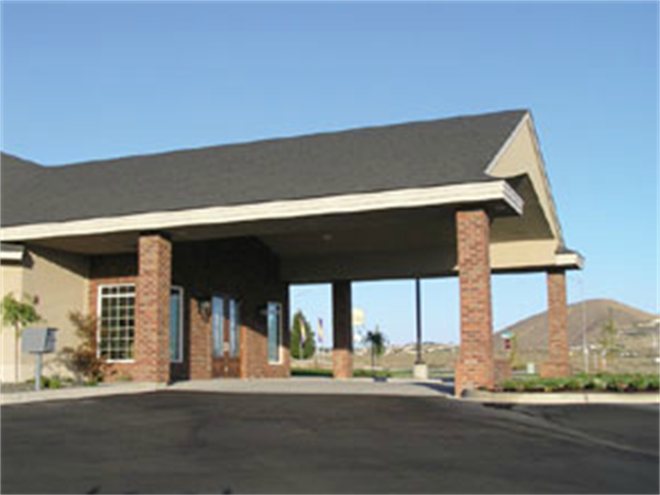 Covered driveway entrance with brick columns and a dark roof under a clear blue sky