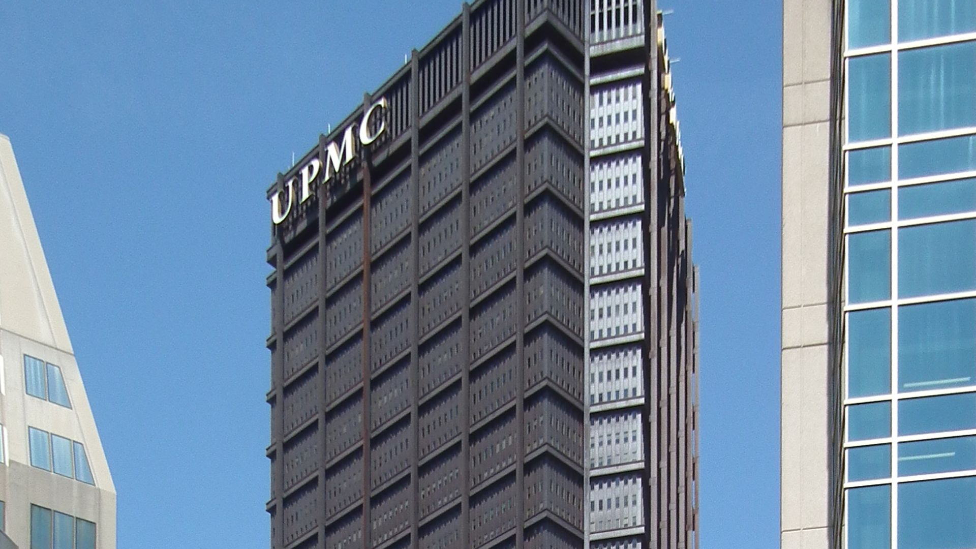Low-angle view of a dark, curved skyscraper with a repetitive grid facade against a cloudy sky.