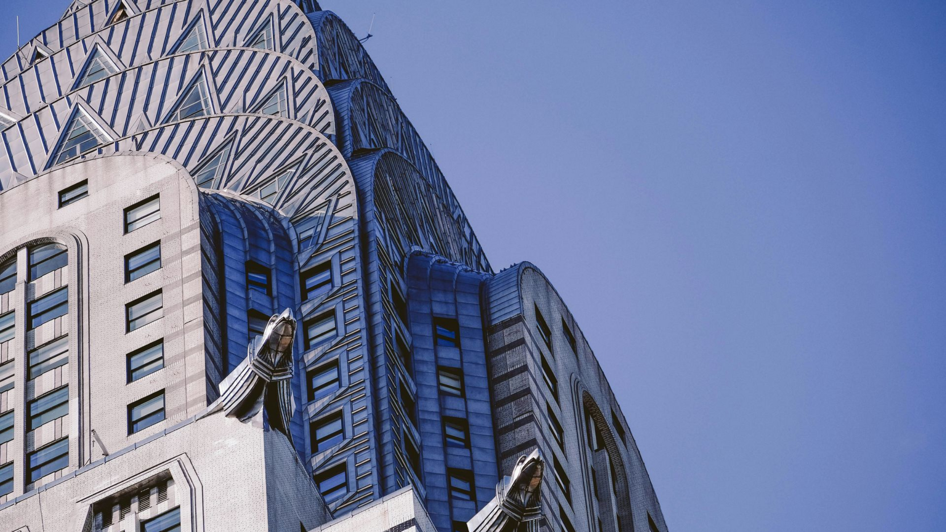 The iconic Art Deco spire of the Chrysler Building in New York City against a clear blue sky.