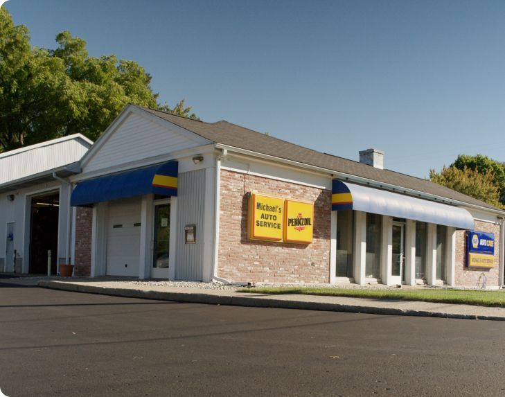 Small brick storefront with blue awnings and yellow signage on a sunny street corner. | Michael's Auto Service