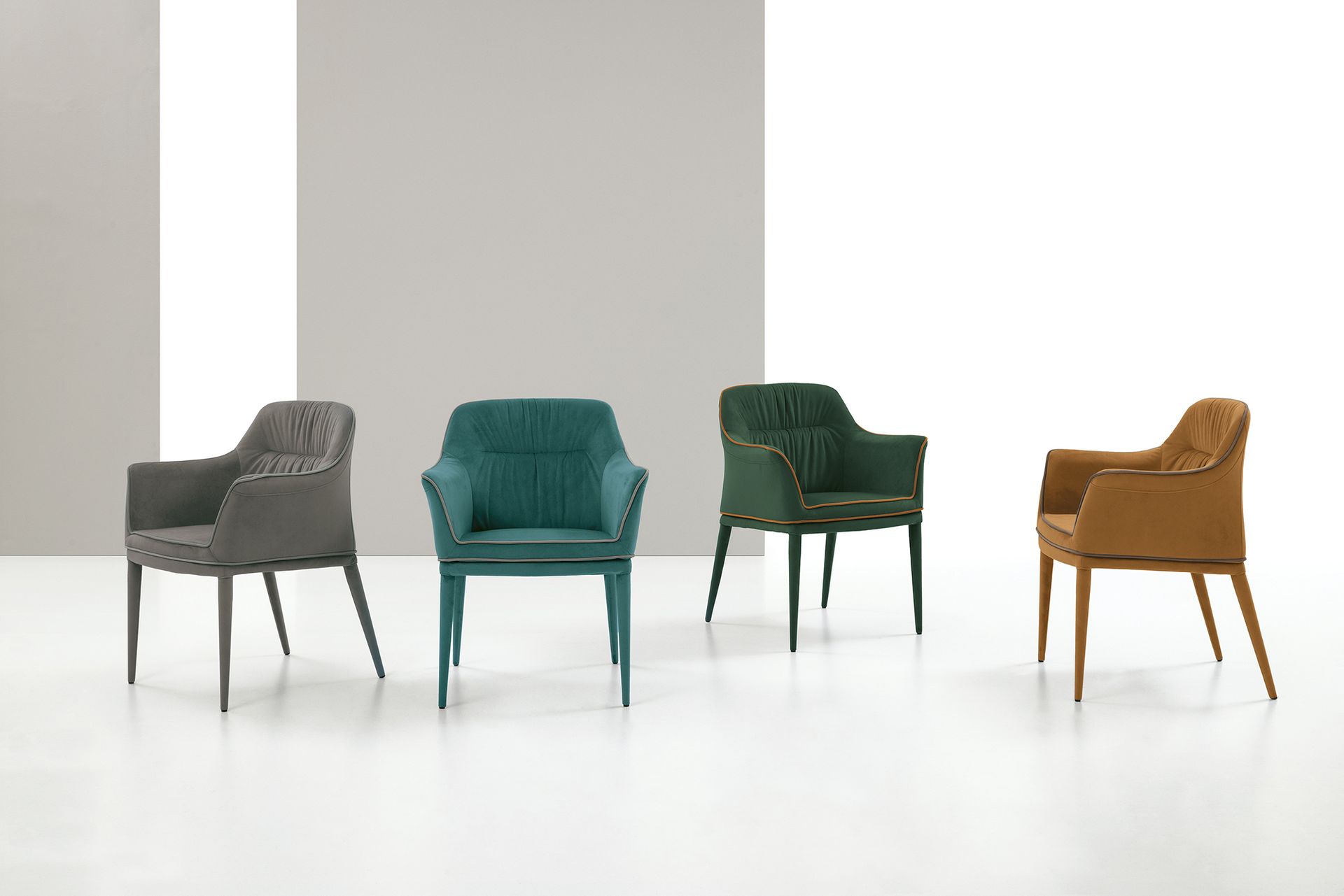 Quattro poltrone imbottite nei colori grigio, verde acqua, verde scuro e marrone chiaro con gambe in metallo su uno sfondo semplice.