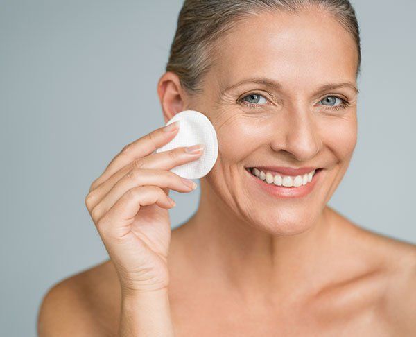 Woman smiles while applying a cotton pad to her face.