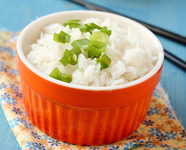 Small orange bowl of white rice topped with chopped green onions, chopsticks beside.