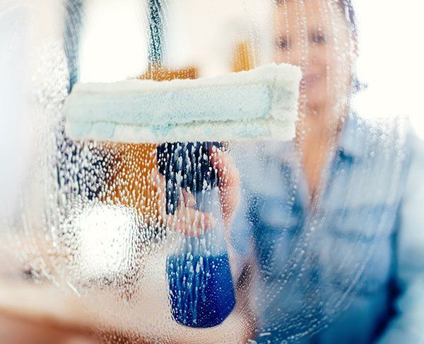 Person sprays window with blue cleaning solution and uses a squeegee.