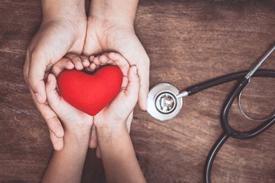 Hands holding a red heart with a stethoscope on a wooden table