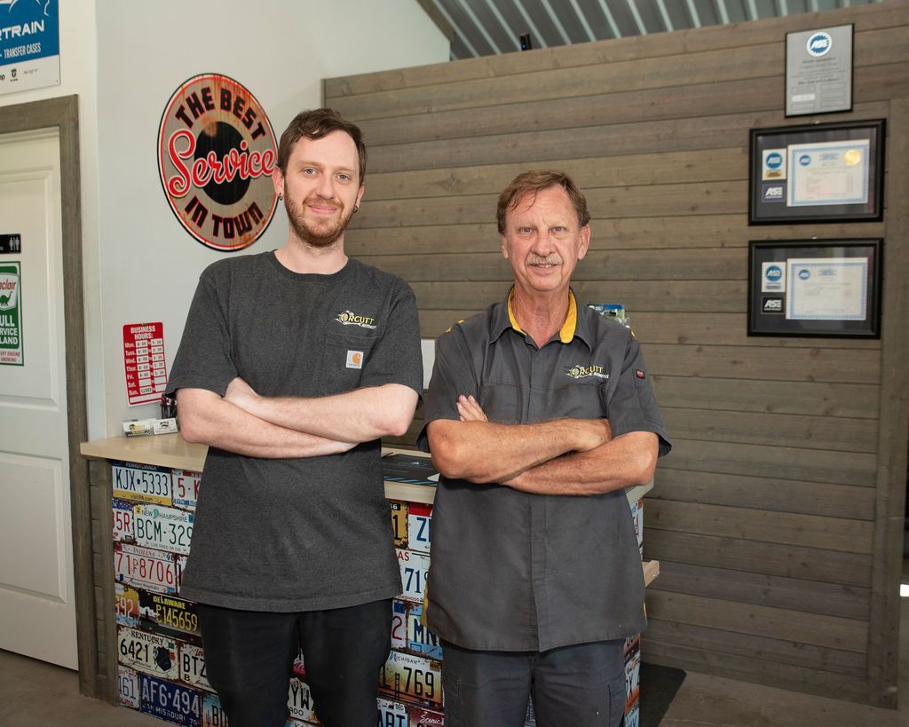 Two men in dark shirts stand with arms crossed in a shop or office lobby