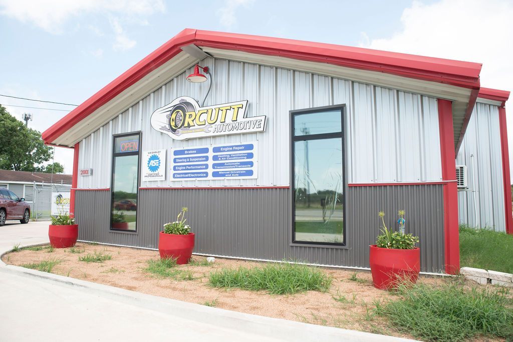 Small roadside storefront with red trim, metal siding, and potted plants by the entrance.