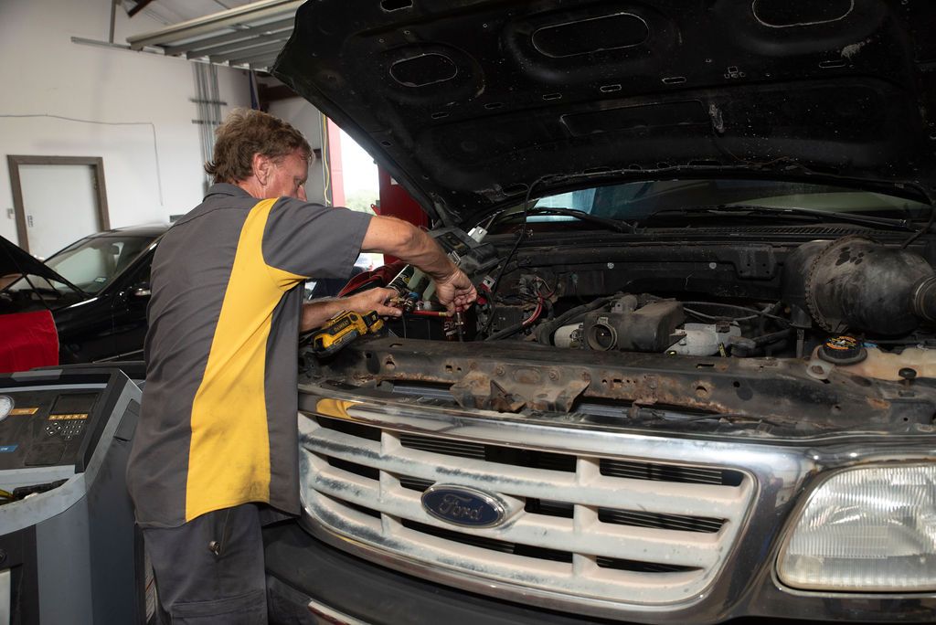 Mechanic working on the engine of a silver Ford SUV in a garage