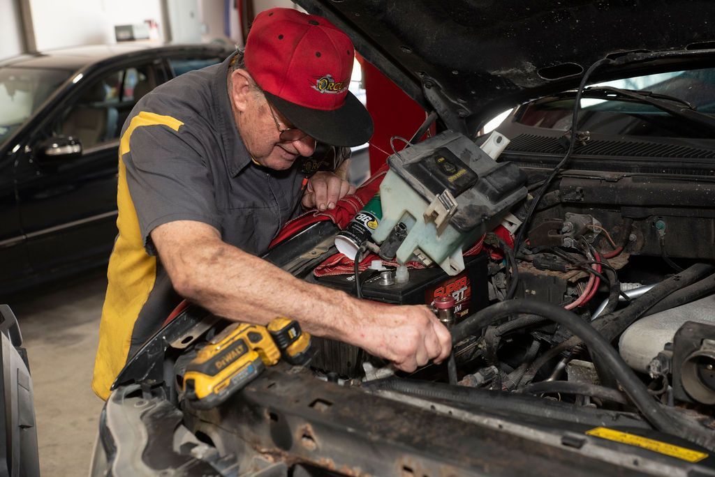 Mechanic working under an open car hood with tools in a garage