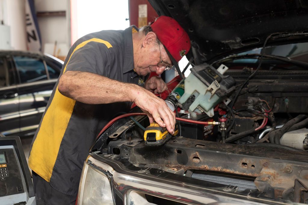 Mechanic working under a car hood with tools in a repair garage