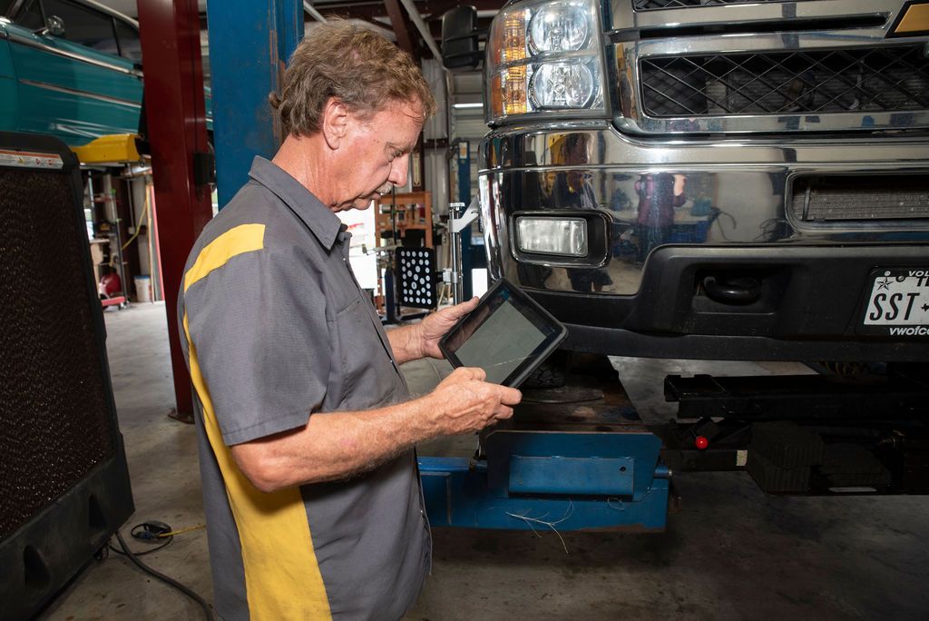 Mechanic using a tablet to inspect the front of a large truck in a garage
