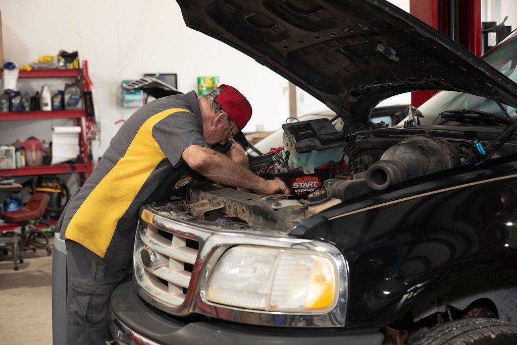 Mechanic working under an open hood of a black SUV in an auto shop