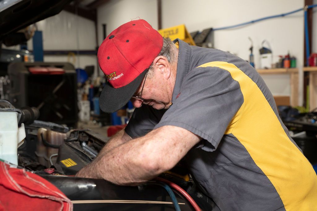 Mechanic in red cap working under a car hood in a garage
