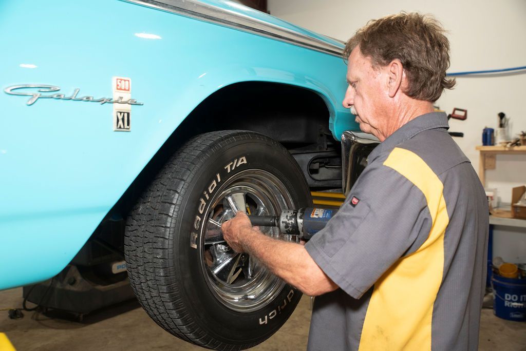 Mechanic tightening a car wheel in a garage beside a light blue vehicle