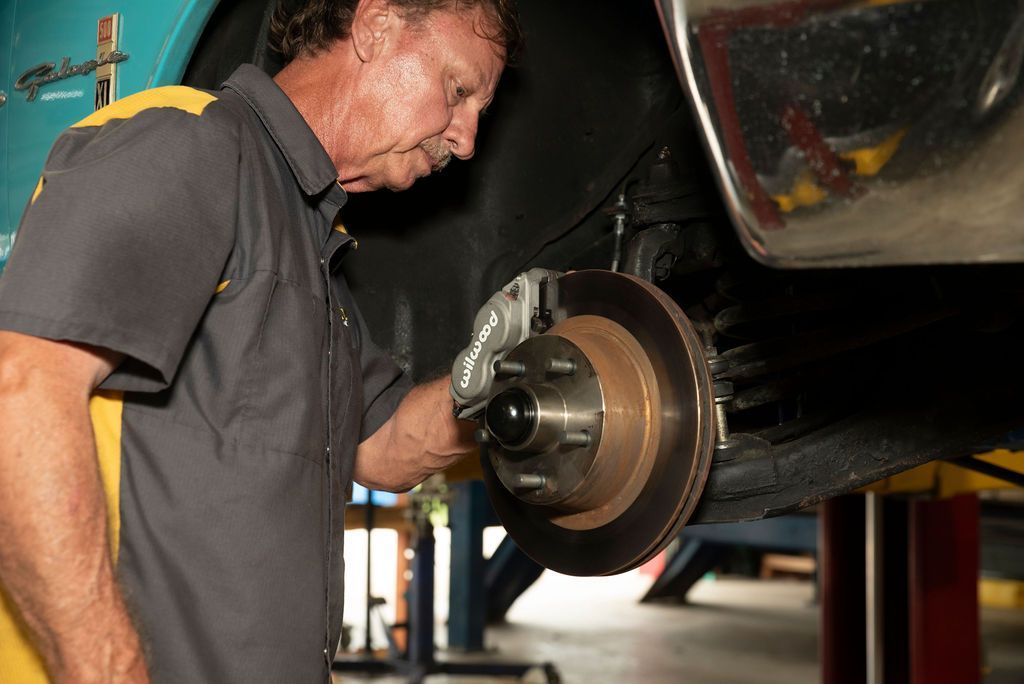 Mechanic inspecting a car brake rotor under the raised vehicle.
