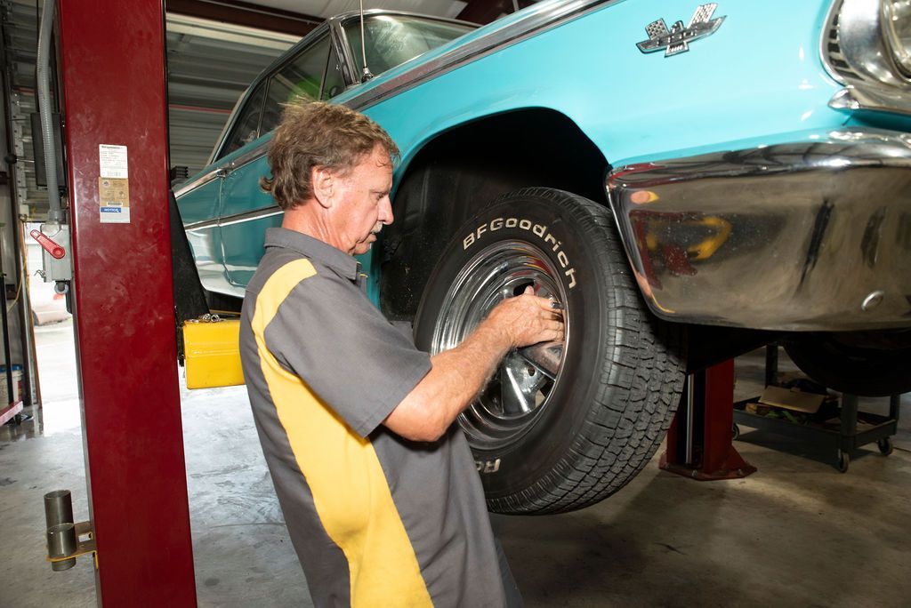 Mechanic working on a turquoise classic car’s front wheel in a garage