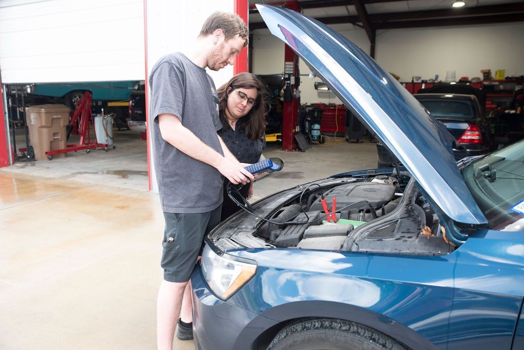 Two people inspecting a blue car with the hood open in a garage