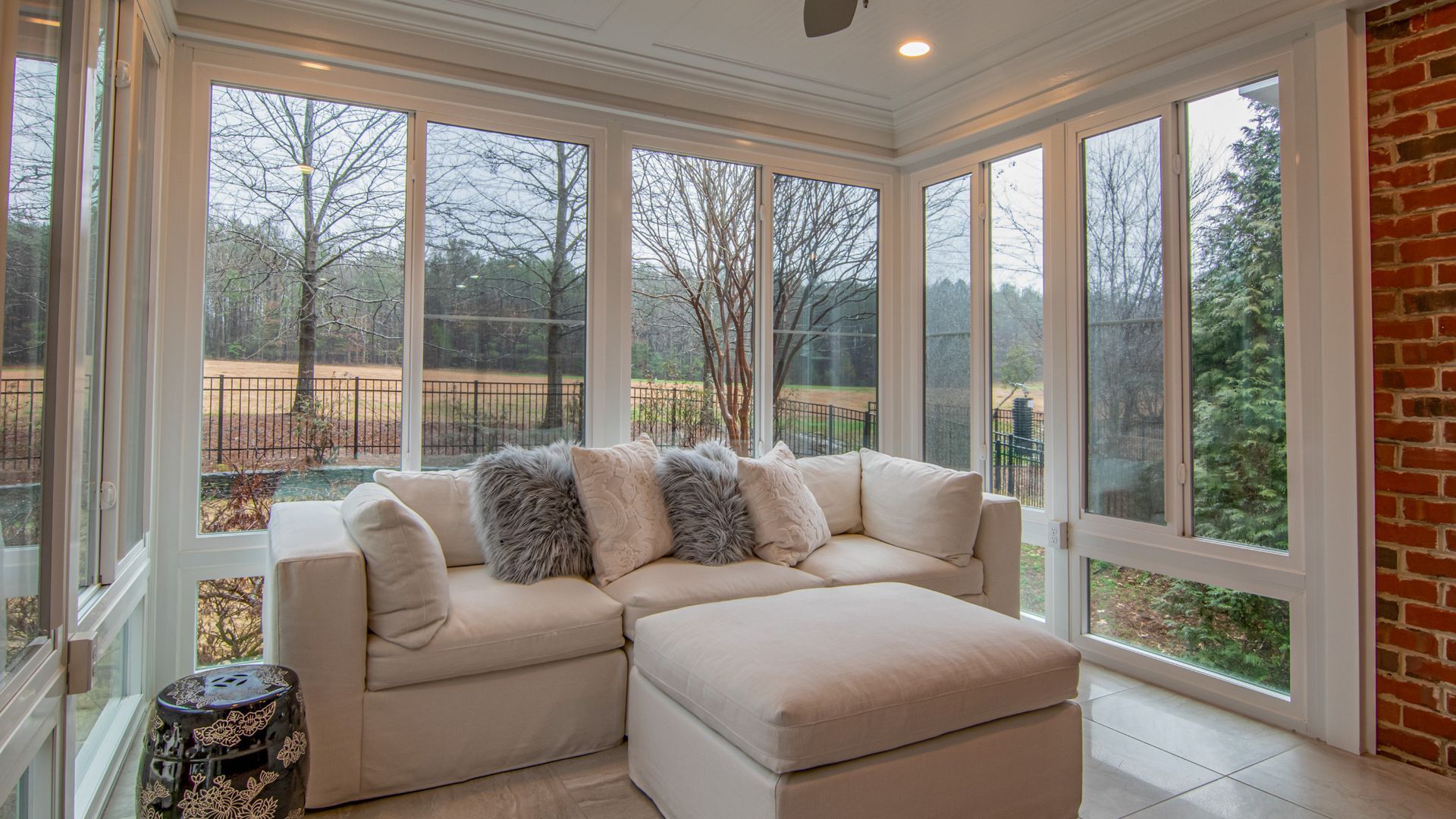 A living room with a couch , ottoman , and lots of windows.
