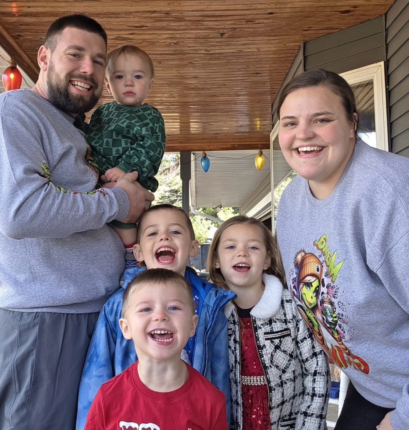 Family owned business of five smiling on a porch, with two adults and three young children in casual clothes.