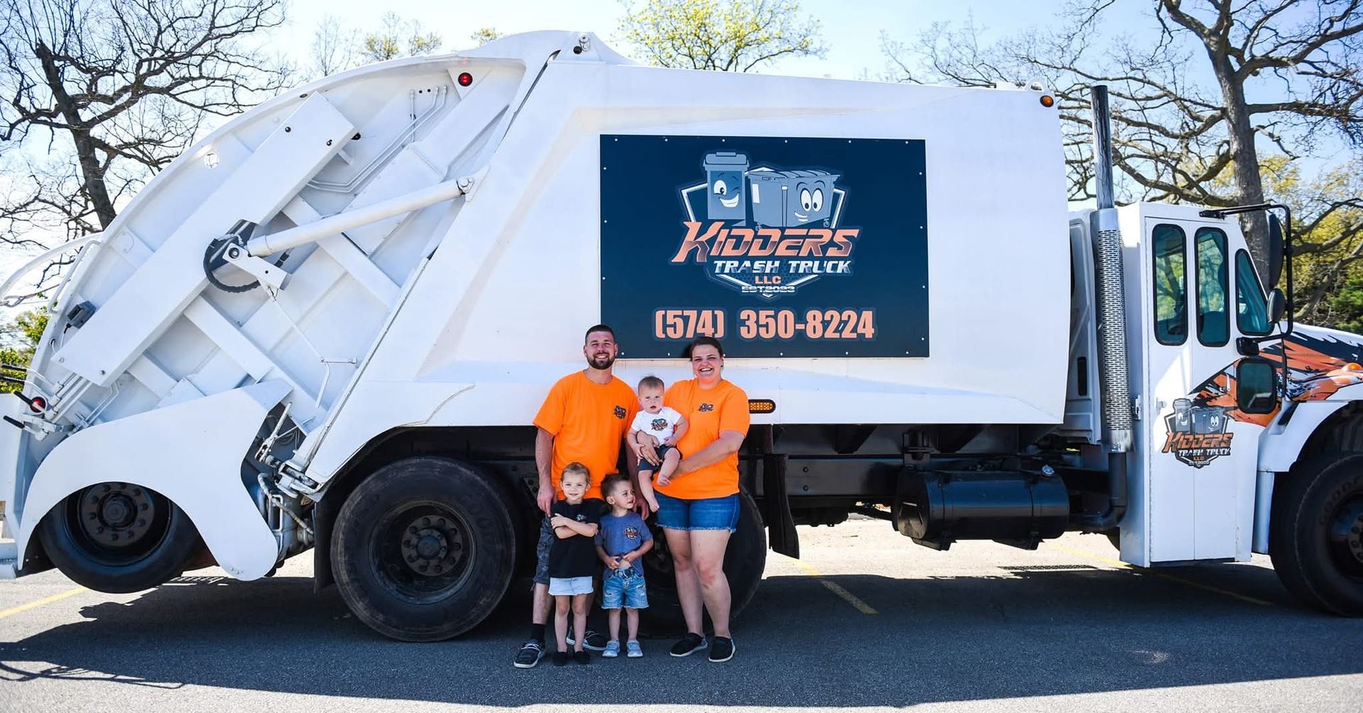 White garbage truck with orange-clad owners posing beside it outdoors