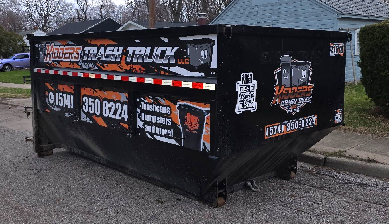 21.5 Yard Dumpster Black with orange-and-white business signage sitting beside a house and basketball hoop, with a red fire hydrant in front.