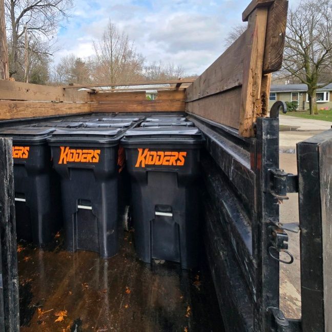 Orange Kidder's dumpster in front of a tan corrugated wall and garage door