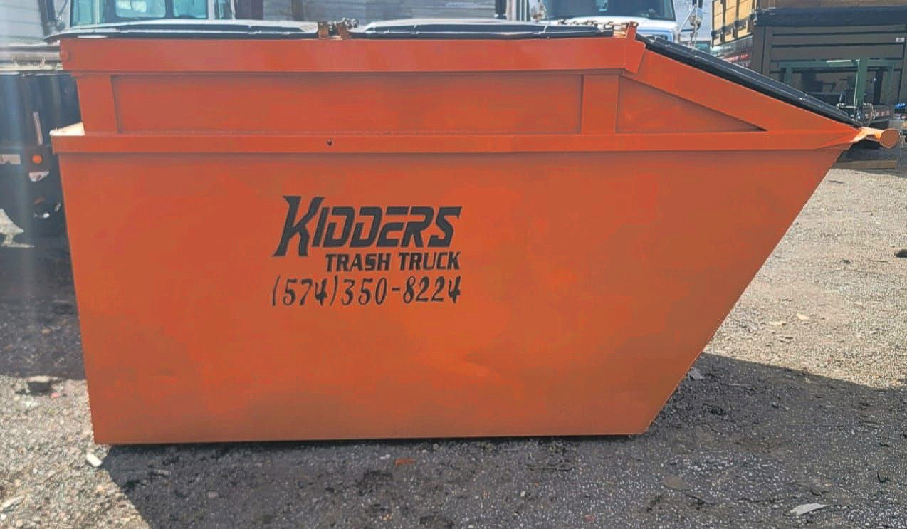 Orange 8 yard dumpster with “Kidders Trash Truck” logo in a gravel lot