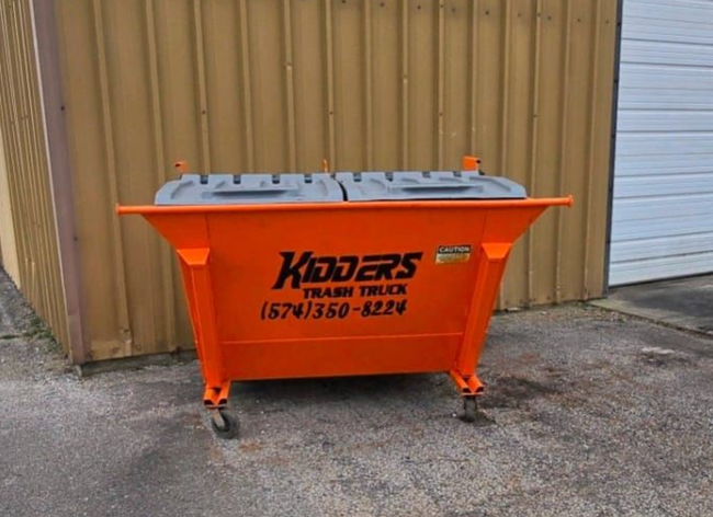 Orange Kidder's dumpster in front of a tan corrugated wall and garage door