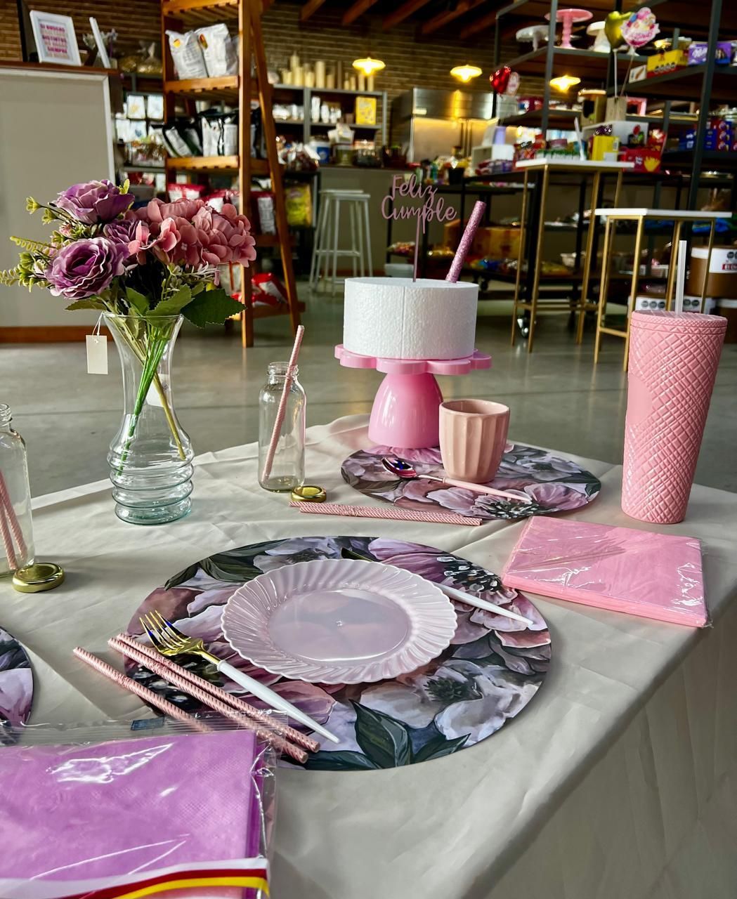 Mesa de fiesta rosa decorada con flores, platos, velas y un centro de mesa con pastel.