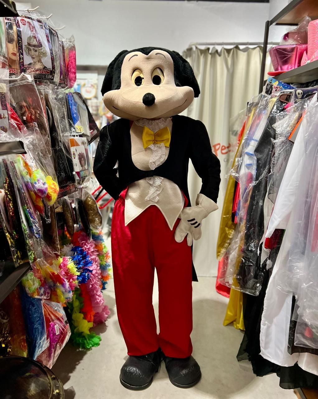 Disfraz de Mickey Mouse de pie en el pasillo de una tienda de ropa, vistiendo una chaqueta de esmoquin