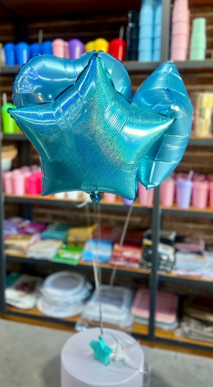 Globo azul brillante con forma de estrella sobre una base blanca en una tienda con coloridas estanterías detrás.