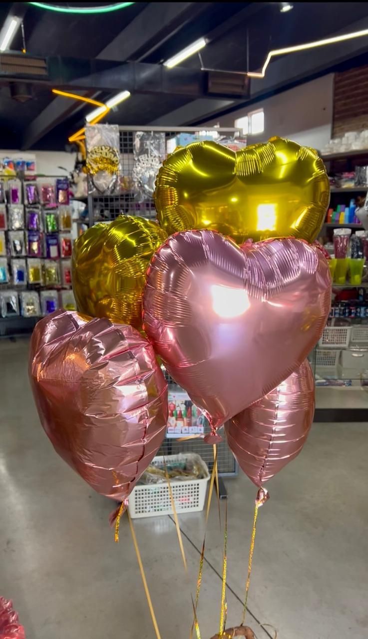 Un grupo de globos brillantes en forma de corazón, de color rosa y dorado, dentro de una tienda.