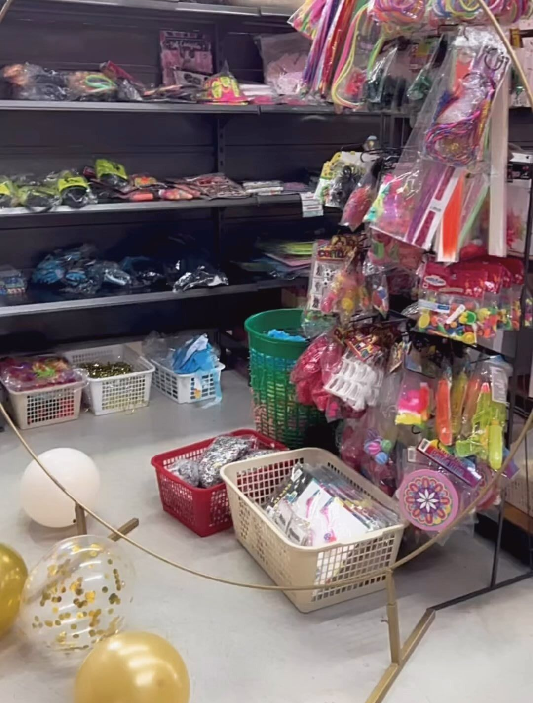 Pasillo de la tienda con coloridas decoraciones colgantes, estantes de juguetes y globos en el suelo.