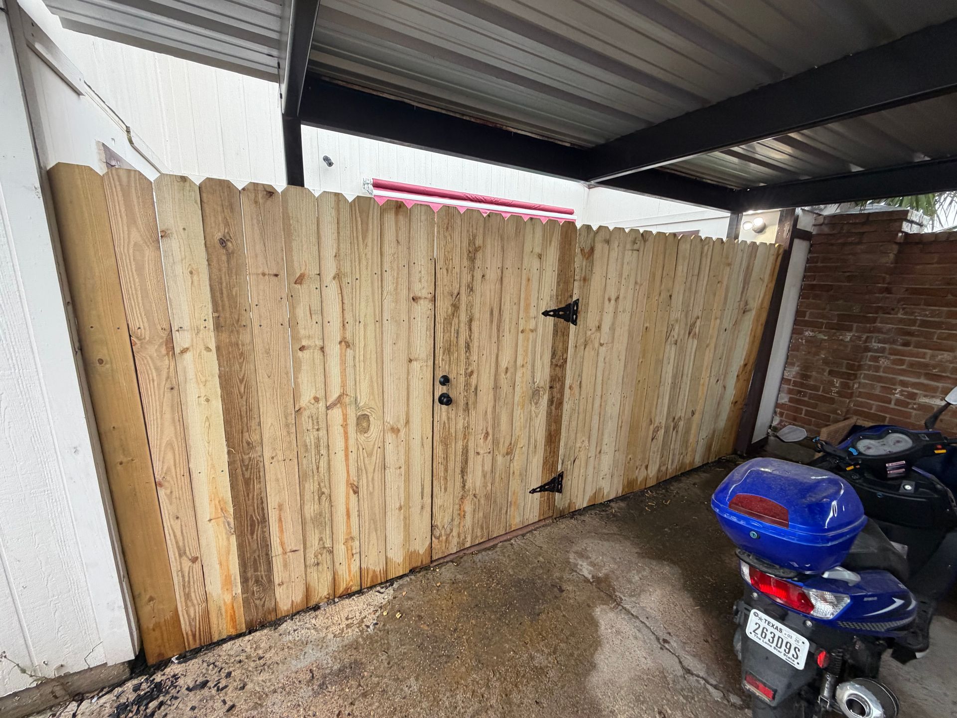 Wooden gate under a covered patio, with a blue scooter parked in the foreground.