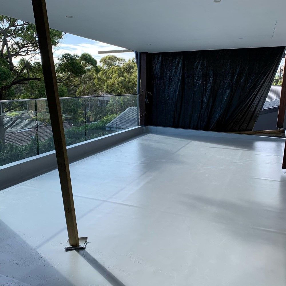 A Balcony With A Glass Railing And Trees In The Background — Coastwide Waterproofing in West Gosford, NSW